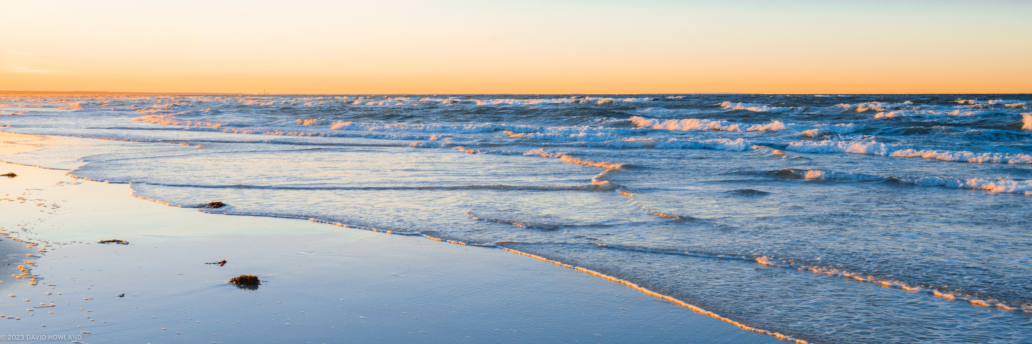 A panorama photo of small waves rolling onto Mayflower Beach at sunset on Cape Cod.