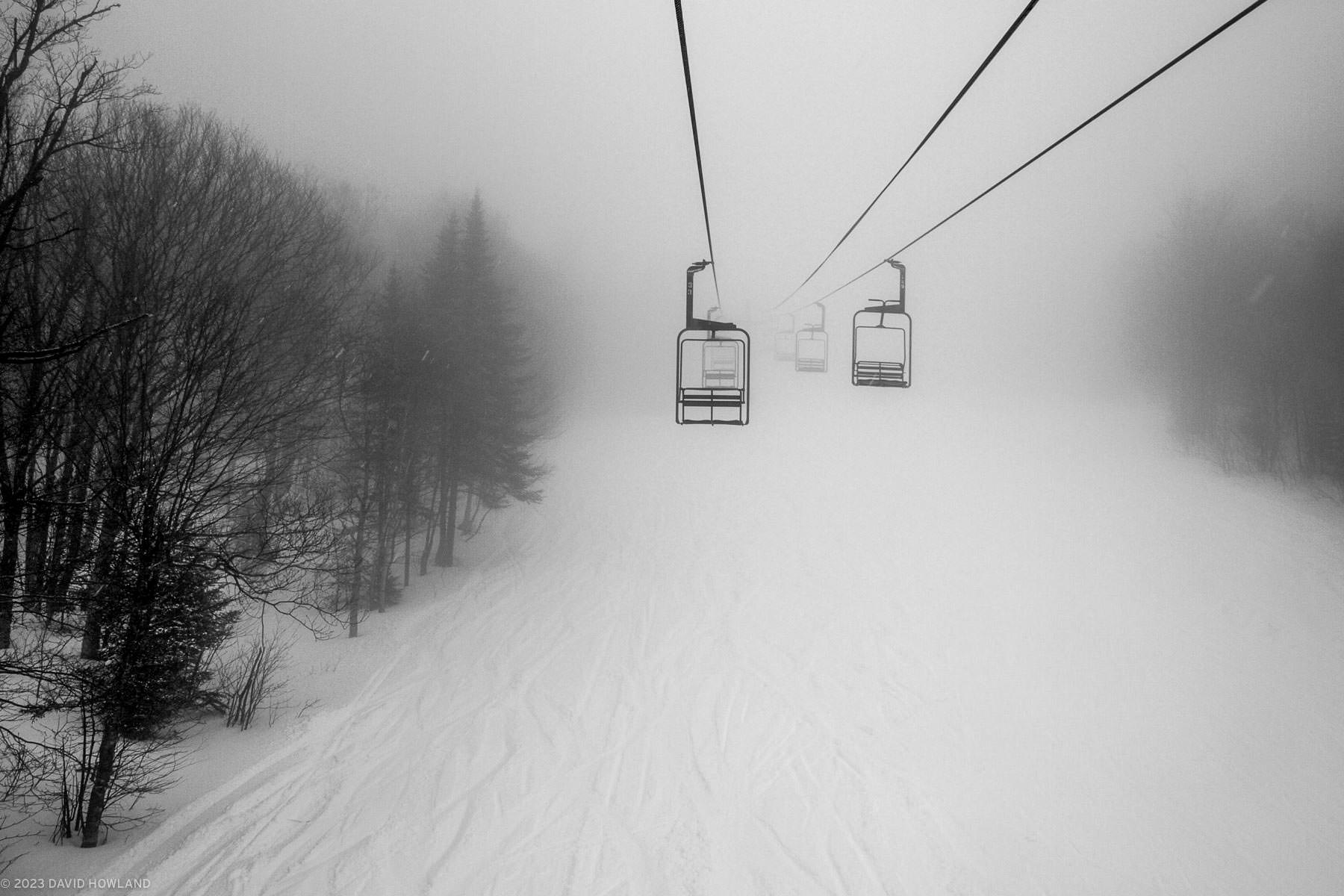 A black and white photo of a chairlift dissapearing into a heavy snowstorm in Vermont.