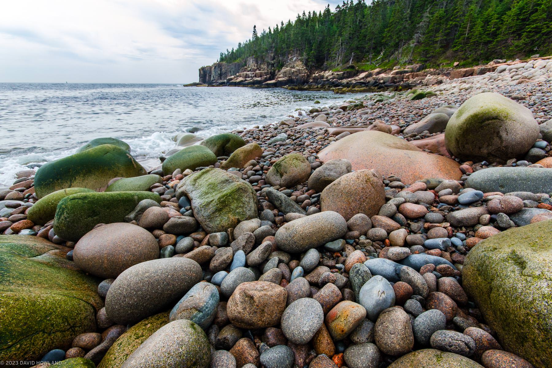 A photo of the waves crashing on the multicolored smooth round boulders on the shores of Acadia National Park in Maine