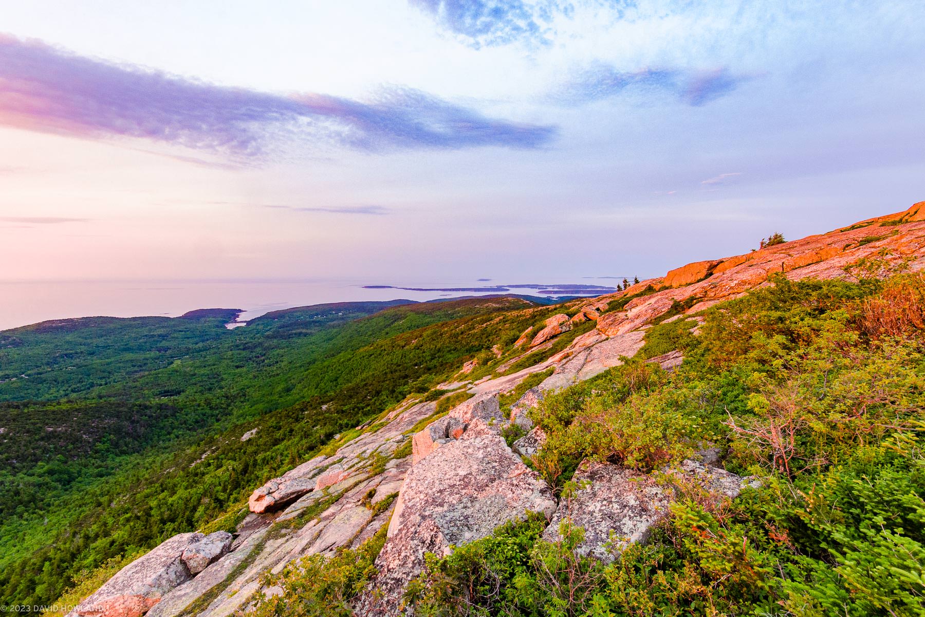 A photo of the sun rising over the the pink granite of the summit of Cadillac Mountain in Acadia National Park, Maine.