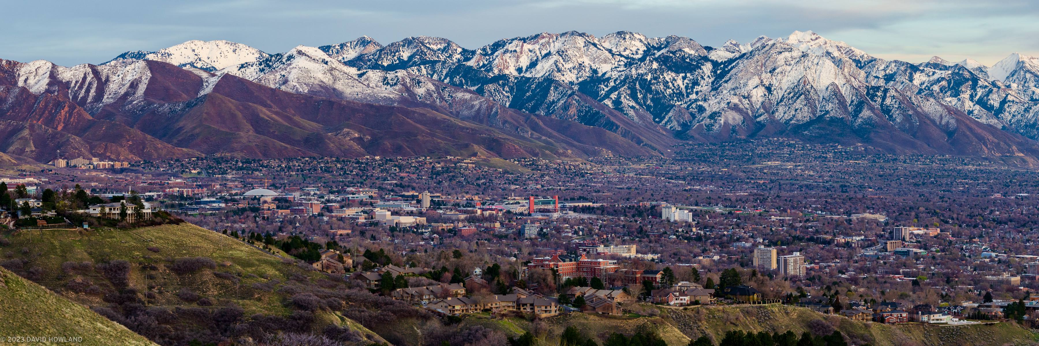A panorama photo of the snow covered Wasatch mountain range rising over the buildings of the University of Utah and the Salt Lake Valley.