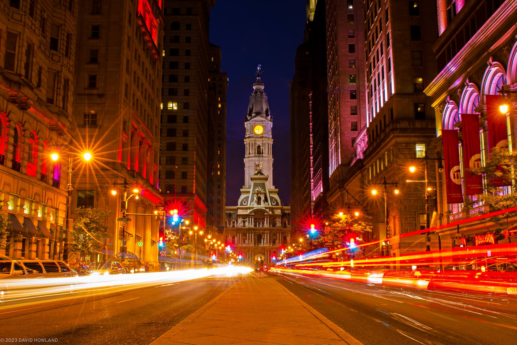 A photo of Broad Street in Center City Philadelphia with the tower of City Hall rising over the median walkway bisecting the busy roadway