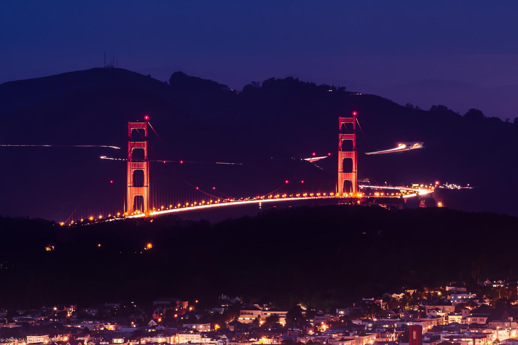 A long exposure photo of the Golden Gate Bridge taken from Twin Peaks with the streams of traffic in the Marin Headlands visible behind the bridge.