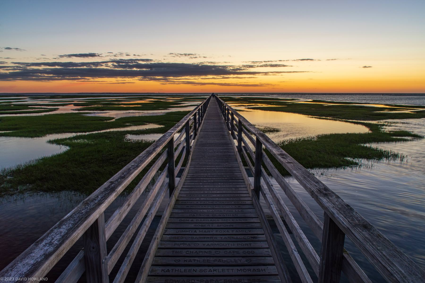 A photo of a colorful orange sunset over the boardwalk at Grays Beach in Yarmouth Port on Cape Cod.