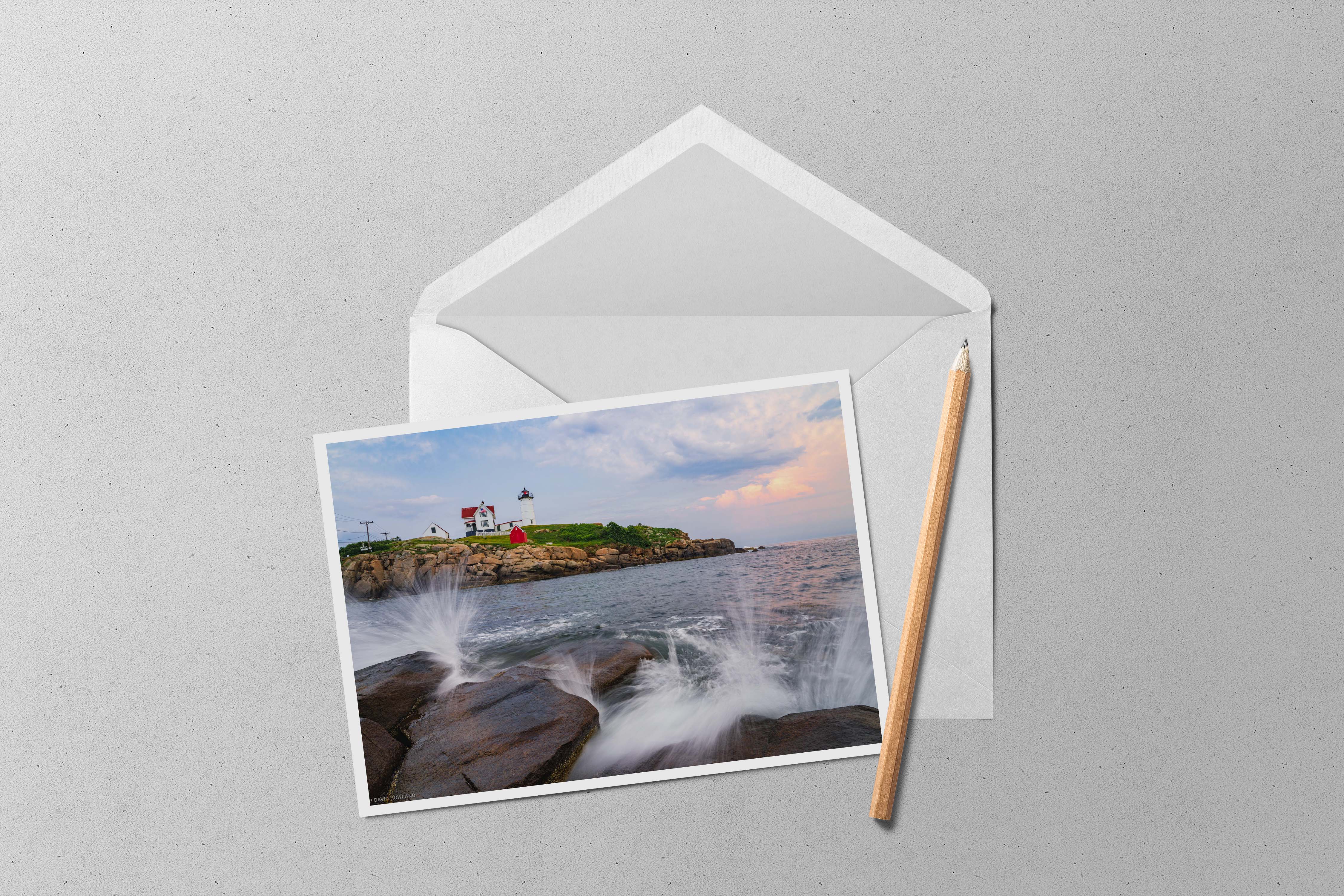 A sunset photo of waves crashing on the rocks of the coast of Maine with Nubble Lighthouse in the background.