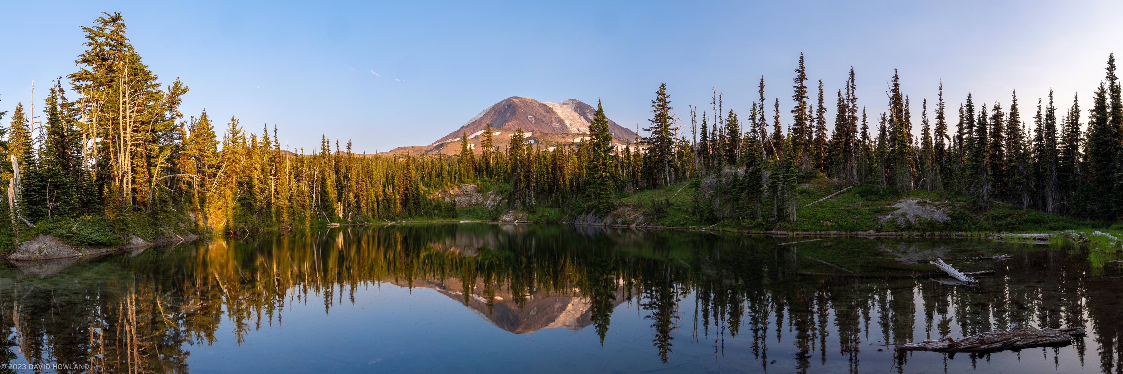 A panorama photo of snow-coverd Mount Adams reflected in the water of an alpine lake at sunset