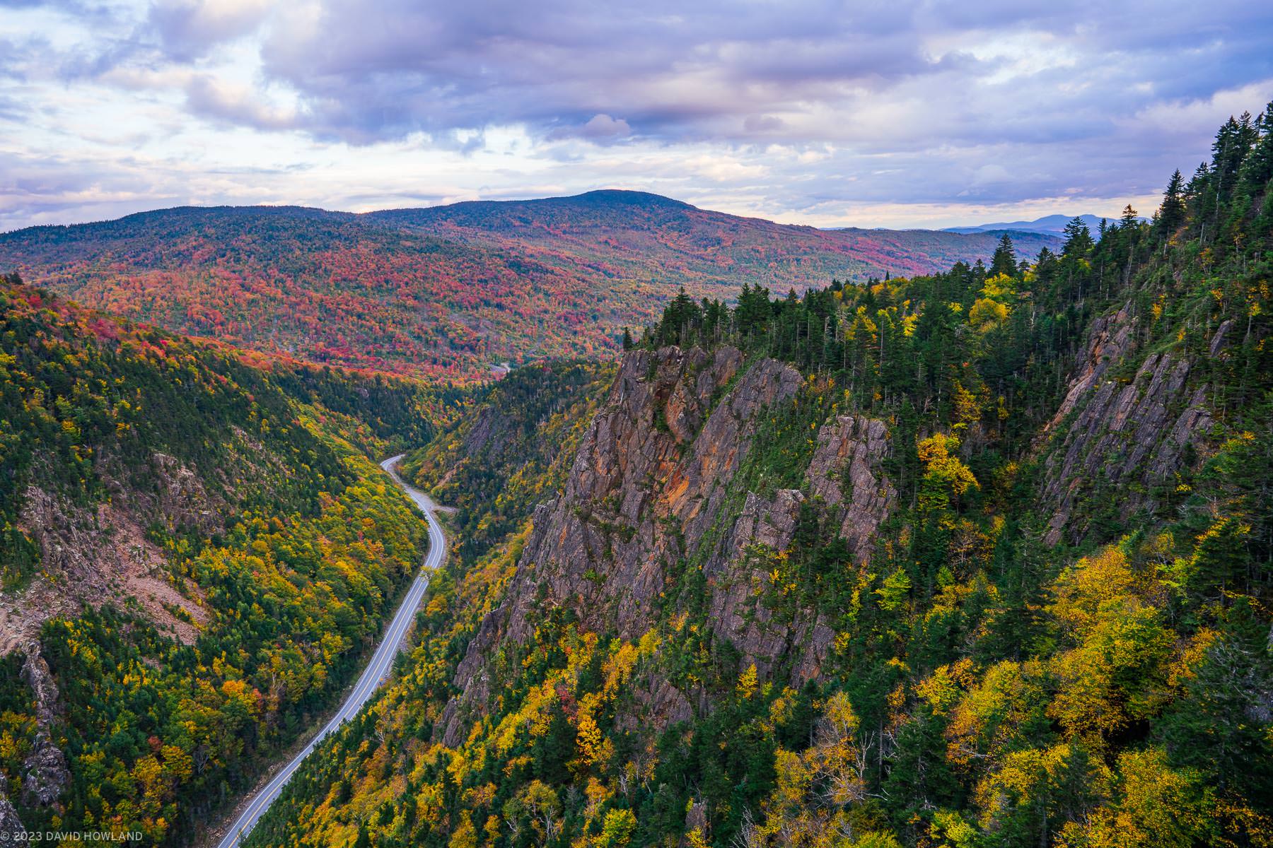 A photo of a road cutting through a steep notch in the mountains of northern New Hampshire at peak fall foliage