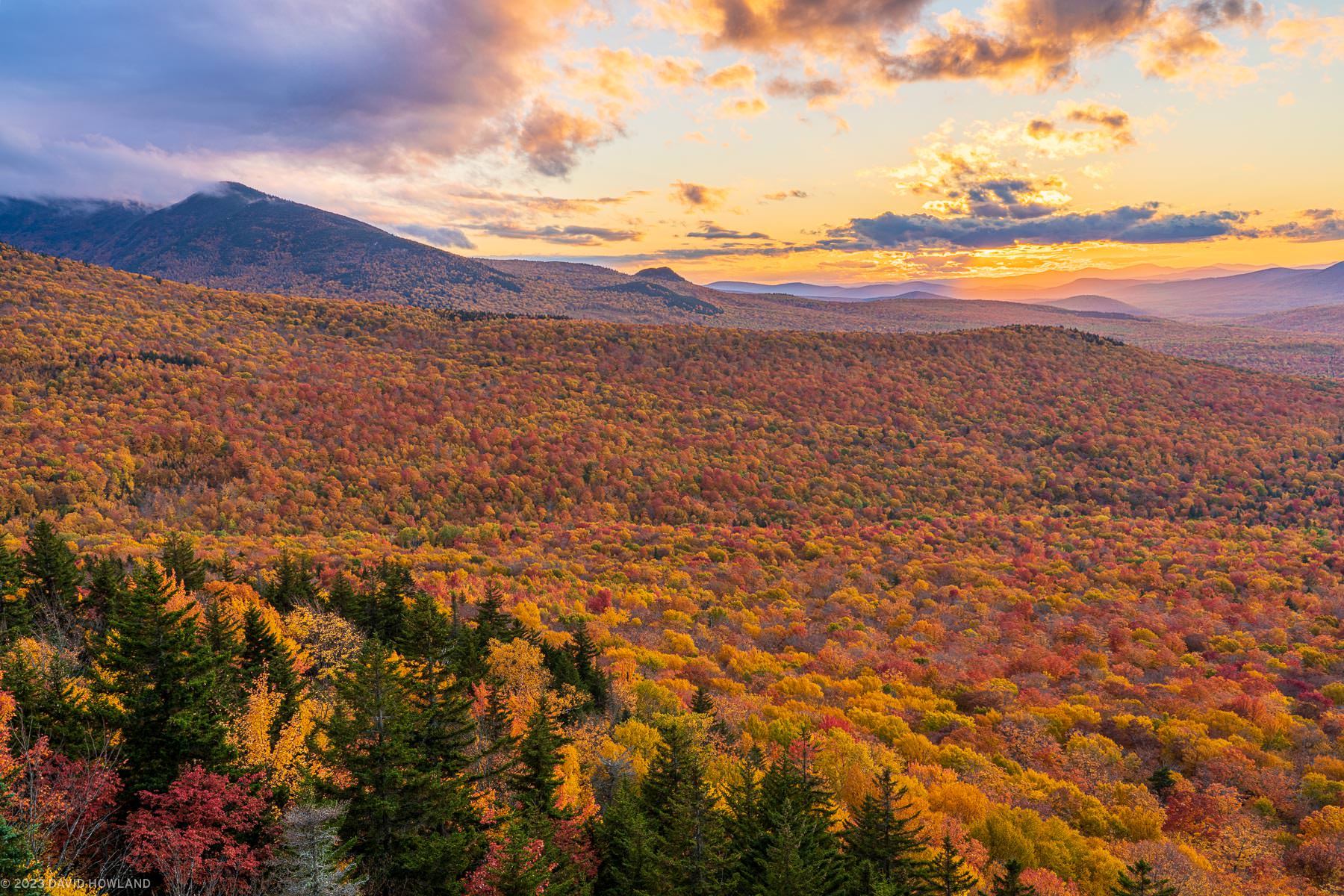 A photo of a colorful orange sunset behind a forest full of fall foliage in the White Mountains of New Hampshire