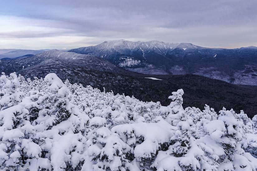 A photo of snowy trees in front of the snow-covered peaks of Franconia Notch in the White Mountains of New Hampshire