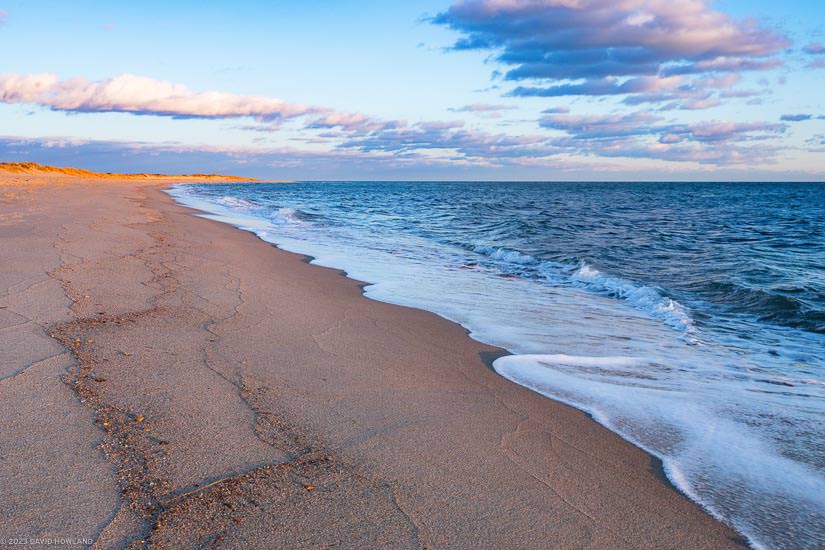 A photo of waves rolling onto a sandy beach at sunset in South Cape Beach State Park on Cape Cod.