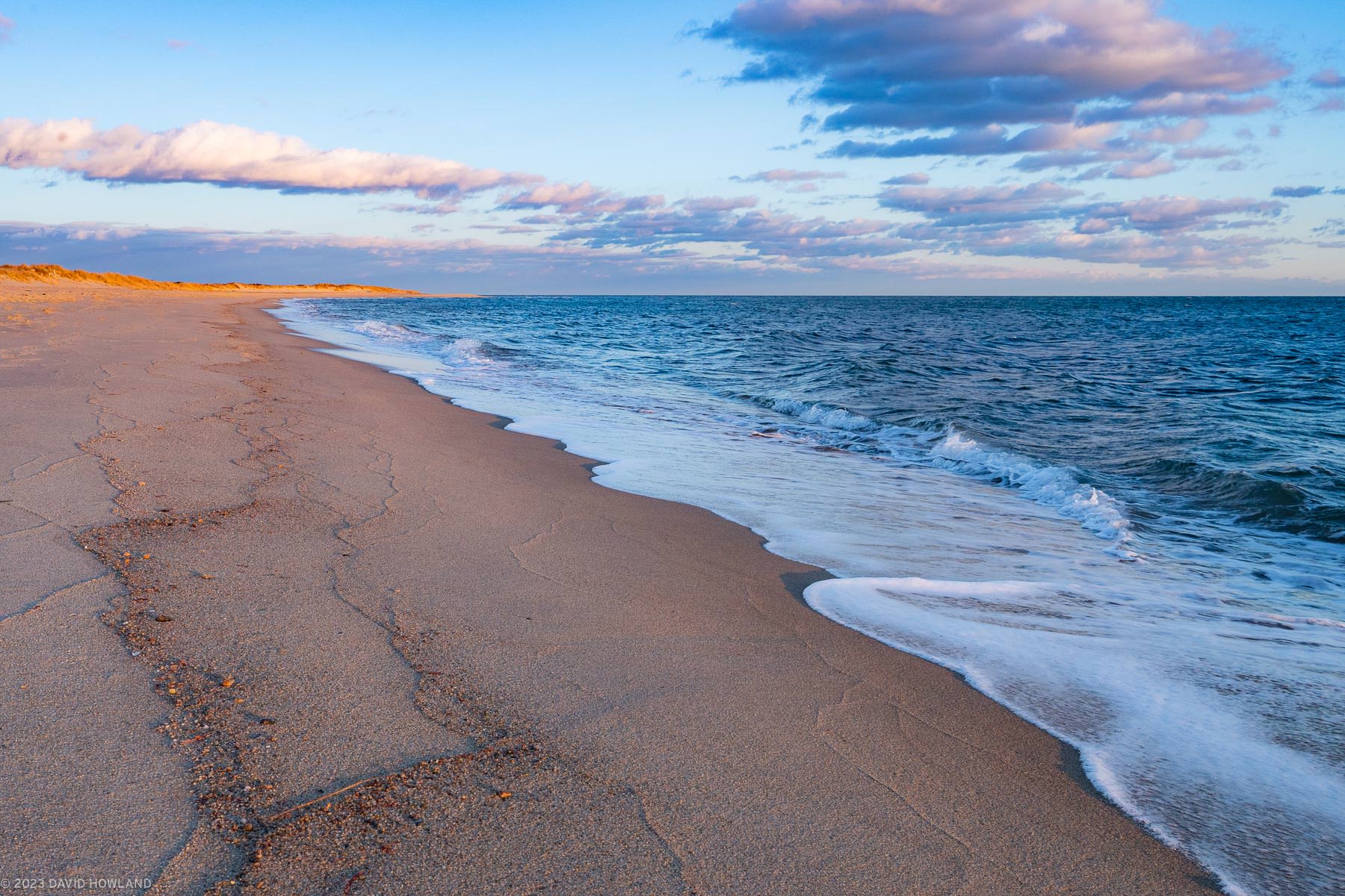 A photo of waves rolling onto a sandy beach at sunset in South Cape Beach State Park on Cape Cod.