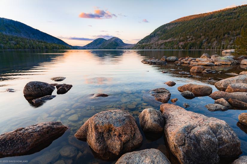 A photo of the mountains of Acadia National Park rising above the calm waters of Jordan Pond at sunset.