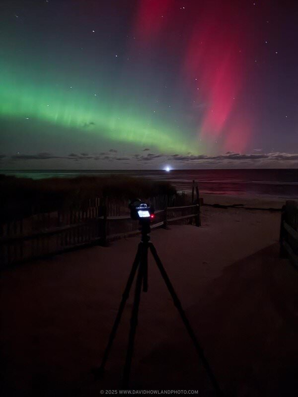 My camera sits on a tripod at Coast Guard Beach while two different bands of aurora glow green and red over the ocean.