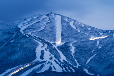 A photo of the ski trails of Cannon Mountain at dusk lit up by the grooming machines traversing the mountain