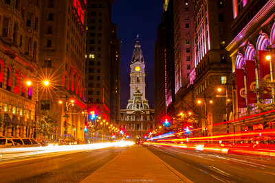 A photo of Broad Street in Center City Philadelphia with the tower of City Hall rising over the median walkway bisecting the busy roadway