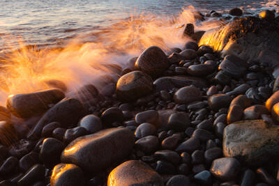 A photo of a waves breaking onto the smooth boulders and granite cliffs of the coastline of Acadia National Park in Maine.