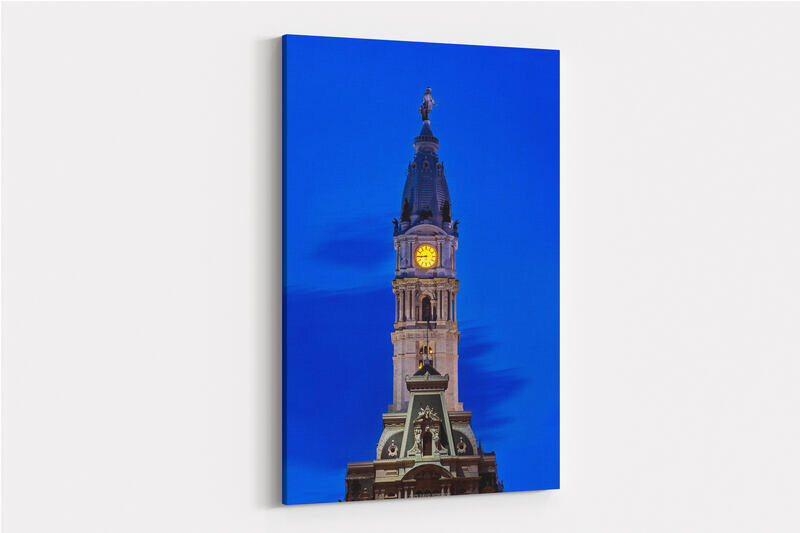 Philadelphia City Hall's ornate tower photographed at dusk, featuring an illuminated yellow clock face and the William Penn statue at its peak, with the building's detailed stonework and green mansard roof lit against a deep blue evening sky.
