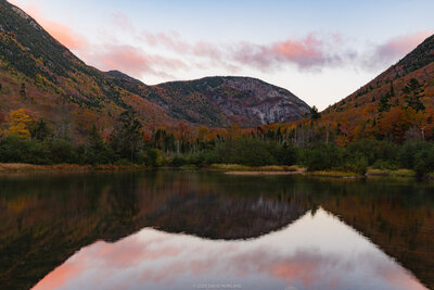 Autumn mountains with colorful foliage reflected in the still waters of Willey Pond at sunrise in Crawford Notch, New Hampshire.