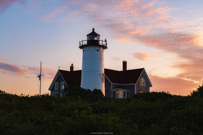 Nobska Lighthouse with attached keeper's house silhouetted against a pink and blue sunrise sky in Woods Hole, Massachusetts.