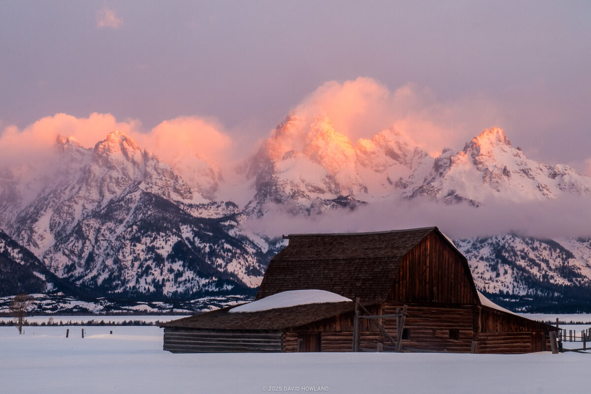 The rocky peaks of the Teton Range glow orange behind Moulton Barn in Grand Teton National Park.