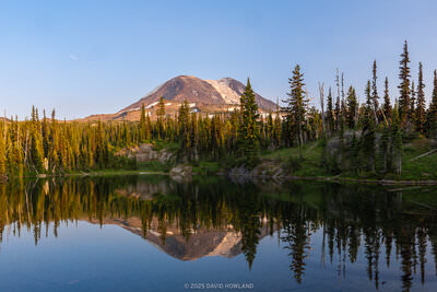 A panorama photo of snow-coverd Mount Adams reflected in the water of an alpine lake at sunset