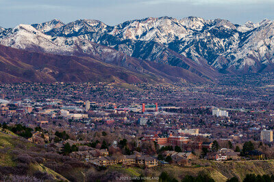 A panorama photo of the snow covered Wasatch mountain range rising over the buildings of the University of Utah and the Salt Lake Valley.