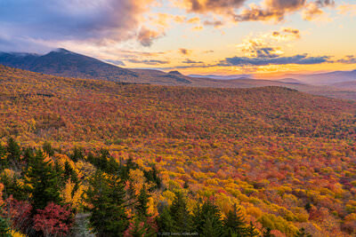 A photo of a colorful orange sunset behind a forest full of fall foliage in the White Mountains of New Hampshire