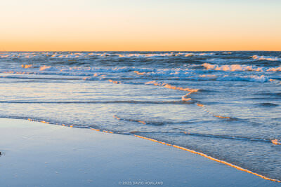 A panorama photo of small waves rolling onto Mayflower Beach at sunset on Cape Cod.