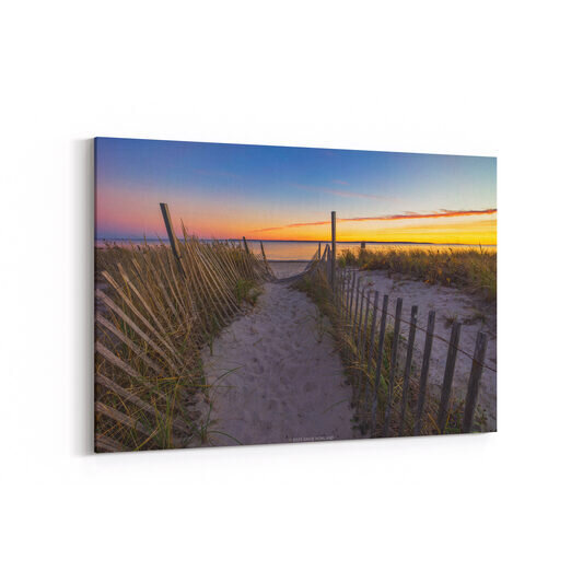 A photo of a battered wooden fence marking a path through the dunes of Surf Drive Beach at sunset in Falmouth, Massachusetts.