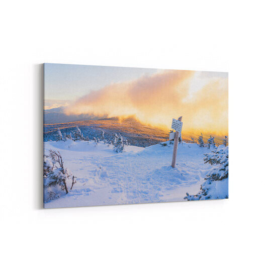 A snow-covered trail junction on the Webster Cliff Trail features a wooden signpost with directional markers, surrounded by frost-laden evergreen trees, with a dramatic golden sunset illuminating billowing clouds over a snow-dusted mountain ridge in the background.