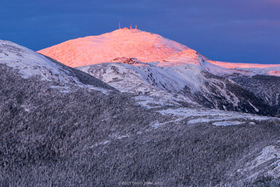 A panorama photo of orange alpenglow lighting up Mount Washington and the other peaks of the Presidential Range in the White Mountains of New Hampshire.