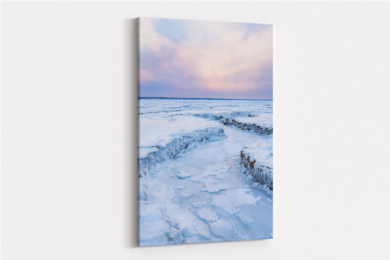 A frozen salt marsh at Bass Hole covered in ice and snow creates winding channels and textured patterns across the landscape, with a soft pink and blue sunset sky reflected in the icy terrain stretching toward the distant shoreline.